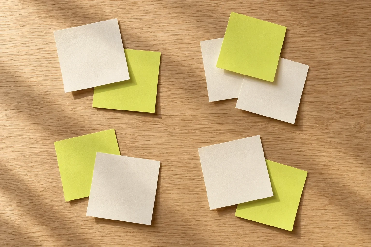 Blank chartreuse and cream sticky notes form four loose clusters on an oak tabletop.