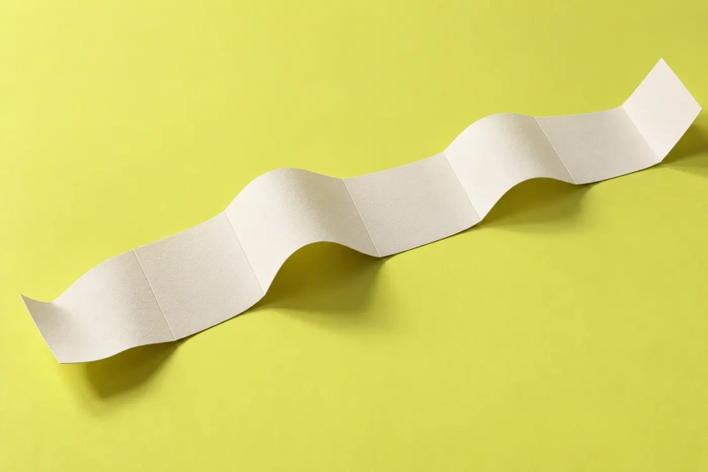A strip of folded paper lying across a chartreuse surface, five panels standing for the working week, with Thursday marked for thinking time.