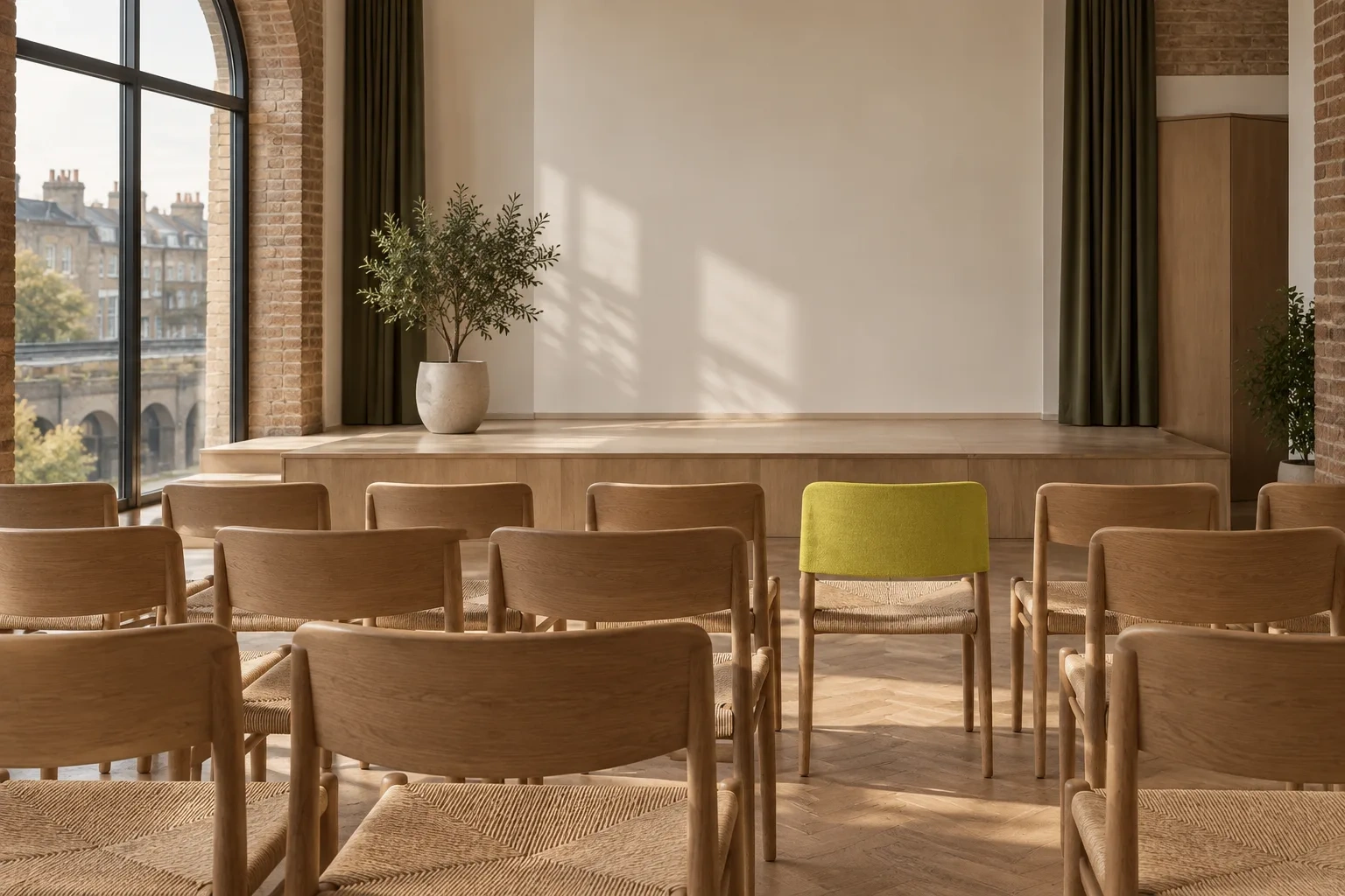 Rows of empty timber chairs face a small stage, with one chartreuse chair cover in front.